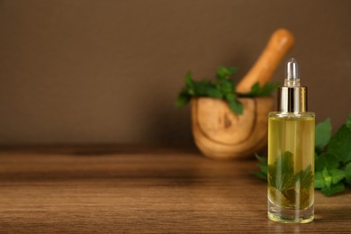 Glass bottle of nettle oil with dropper and leaves on wooden table against brown background, space for text