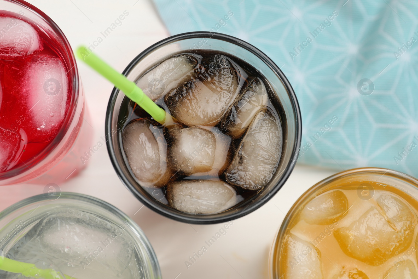 Photo of Glasses of different refreshing soda water with ice cubes and straws on white table, flat lay