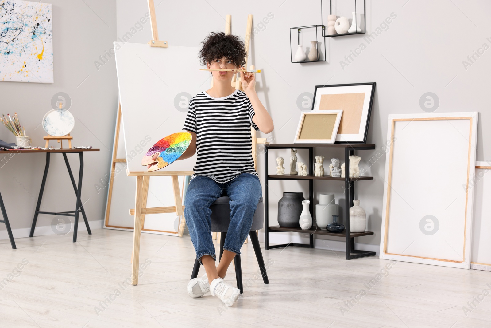 Photo of Young woman with brush and artist`s palette near easel in studio