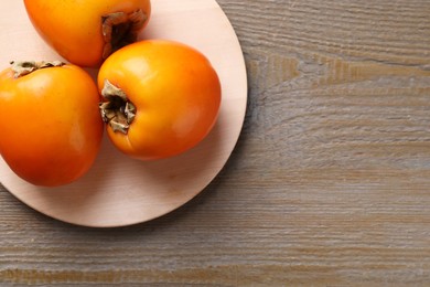 Photo of Delicious ripe persimmons on wooden table, top view. Space for text