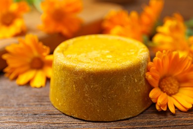 Photo of Yellow solid shampoo bar and flowers on wooden table, closeup. Hair care