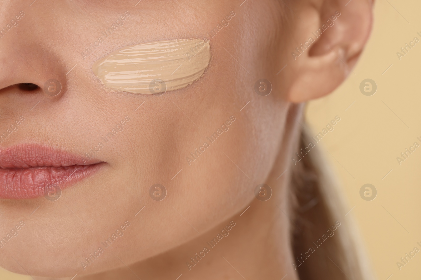 Photo of Woman with swatch of foundation on face against beige background, closeup