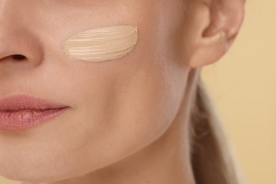 Woman with swatch of foundation on face against beige background, closeup