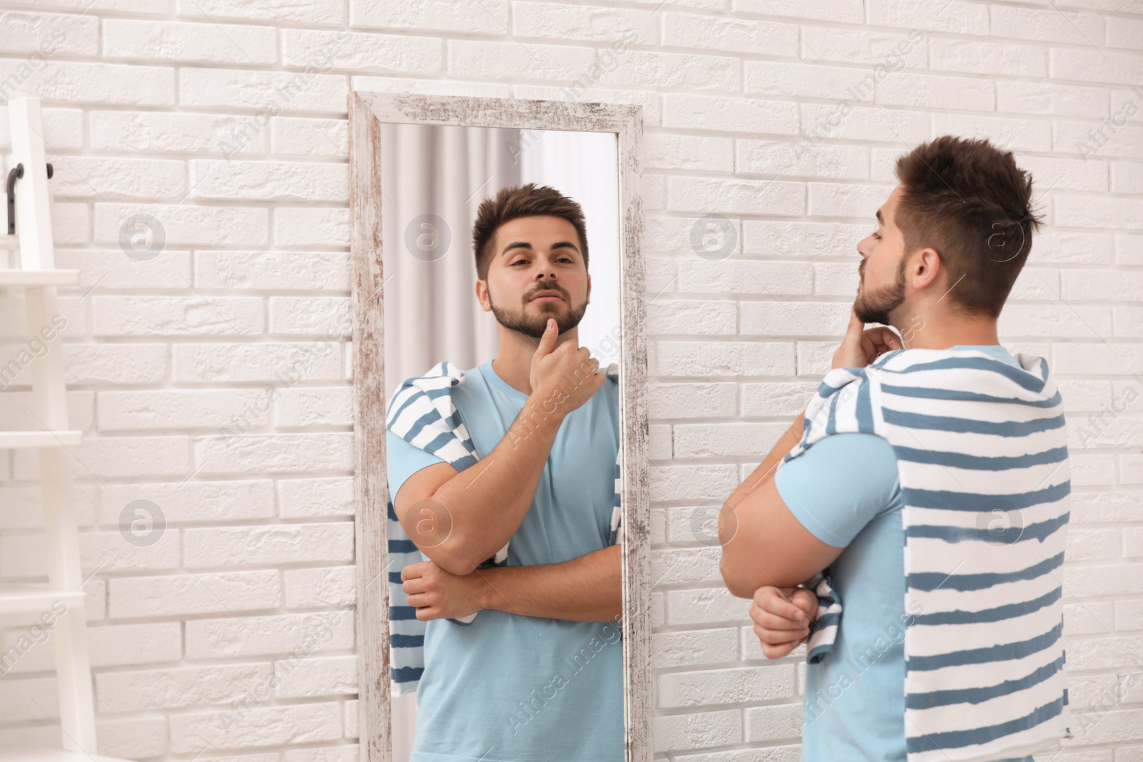 Photo of Young man looking at himself in large mirror at home