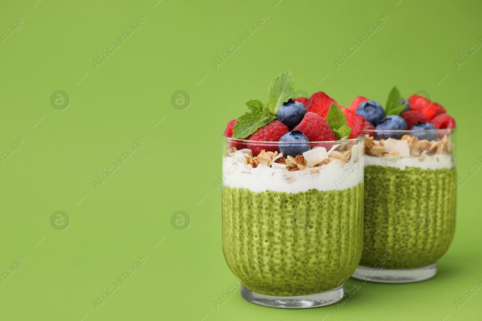 Photo of Tasty matcha chia pudding with oatmeal and berries on green background, space for text. Healthy breakfast