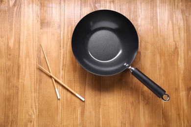 Photo of Empty iron wok and chopsticks on wooden table, top view