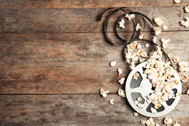 Tasty popcorn and film reel on wooden background, top view with space for text