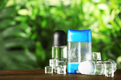 Photo of Set of different deodorants with ice cubes on wooden table against blurred green background
