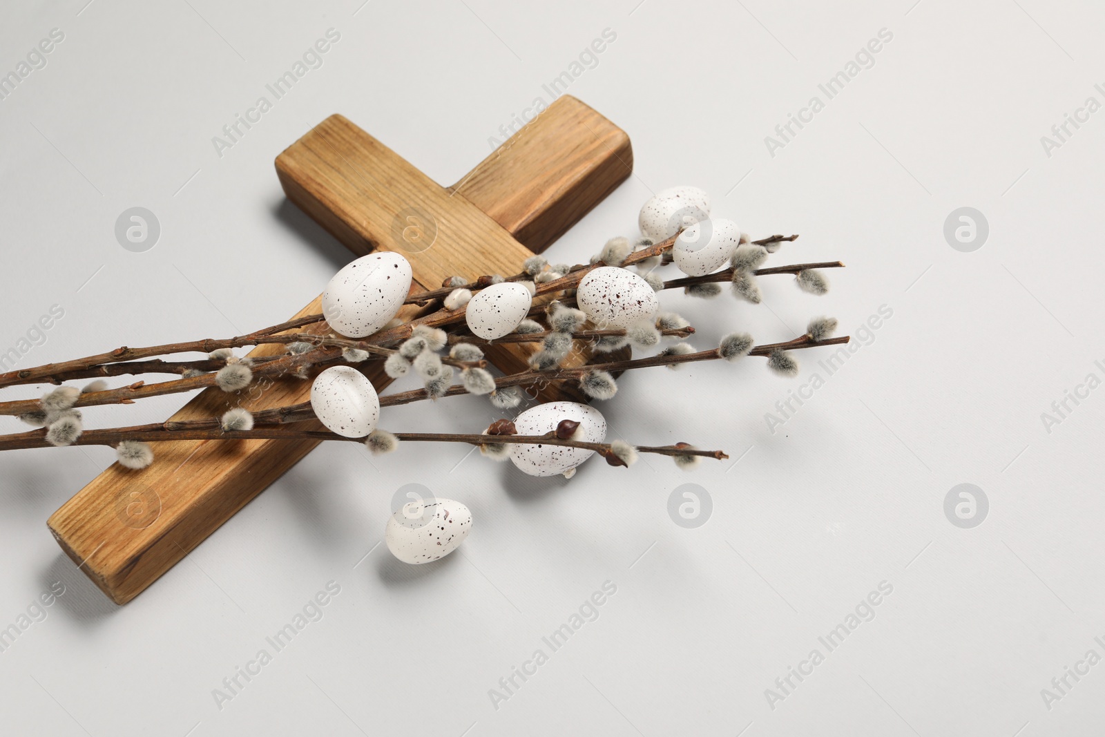 Photo of Wooden cross, painted Easter eggs and willow branches on light grey background, space for text