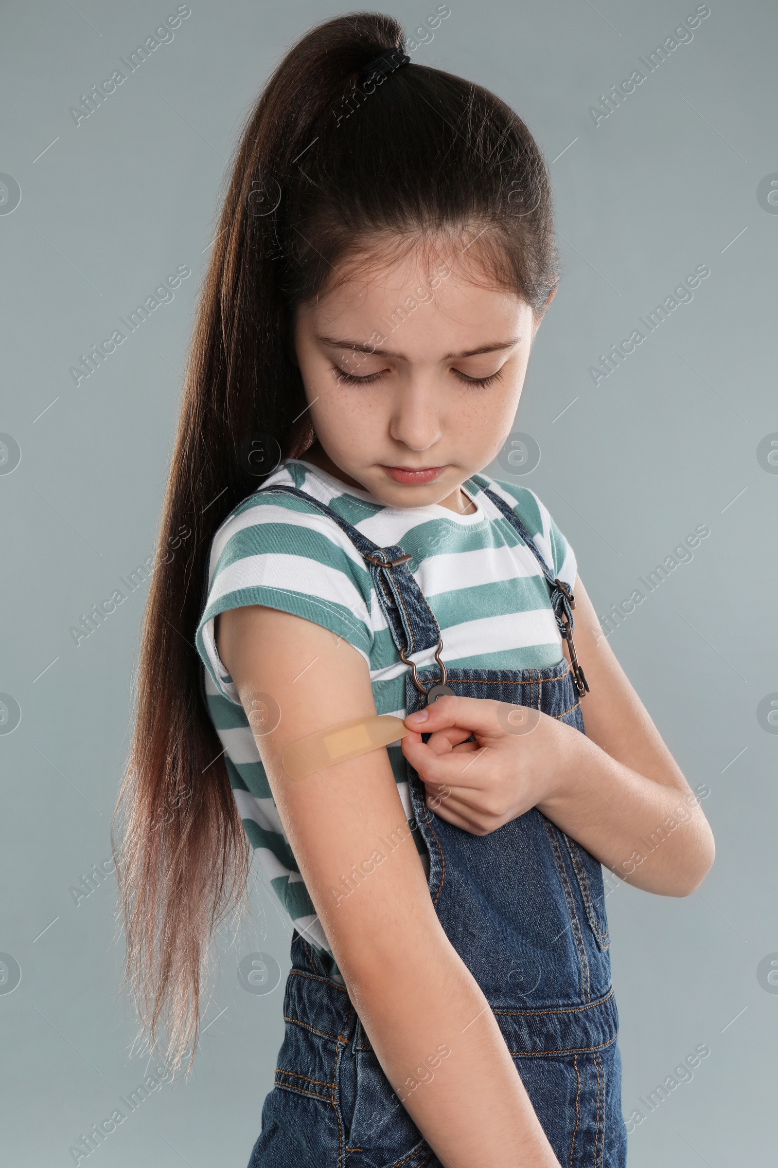 Photo of Girl putting sticking plaster onto arm against light grey background