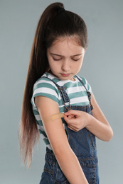 Girl putting sticking plaster onto arm against light grey background