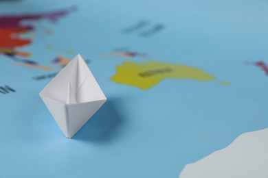 White paper boat on world map, closeup. Space for text