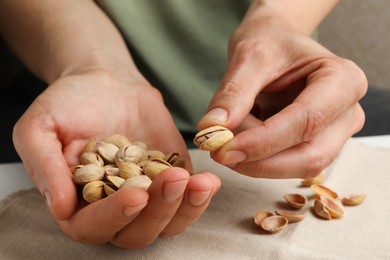 Photo of Woman holding tasty roasted pistachio nuts at table, closeup