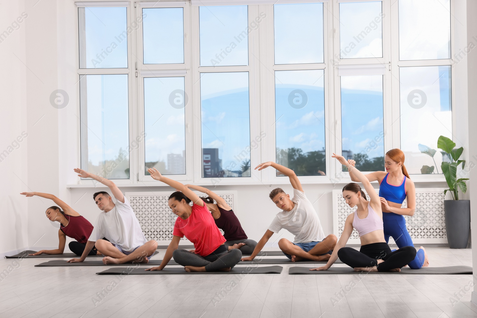 Photo of Yoga coach helping woman during group lesson indoors