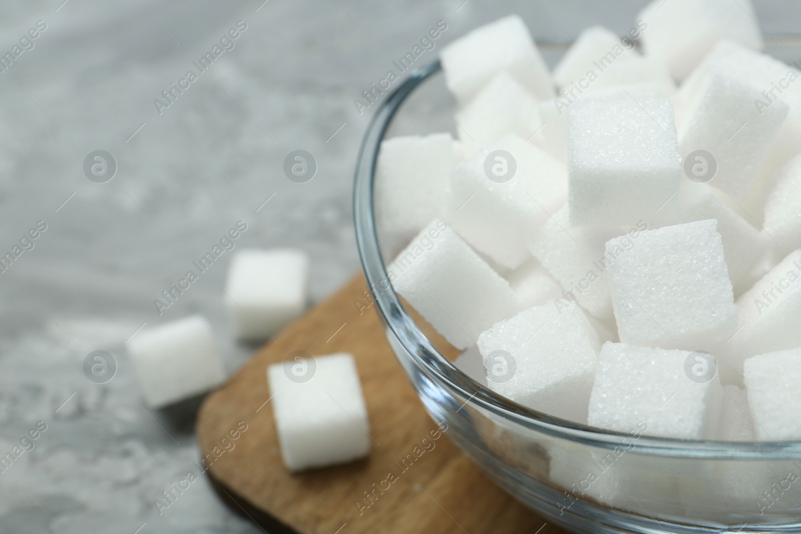 Photo of White sugar cubes in glass bowl on grey table, closeup. Space for text