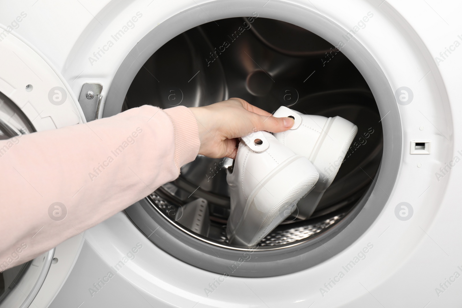 Photo of Woman putting stylish sneakers into washing machine, closeup