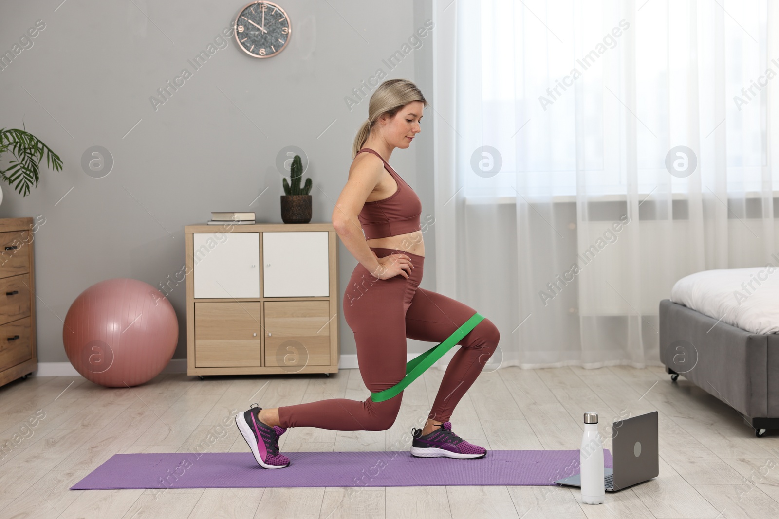 Photo of Online fitness trainer. Woman doing exercise with elastic band near laptop at home