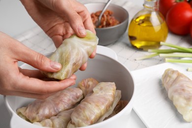 Photo of Woman putting uncooked stuffed cabbage roll into ceramic pot at table, closeup