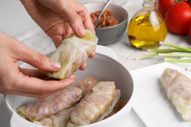 Woman putting uncooked stuffed cabbage roll into ceramic pot at table, closeup