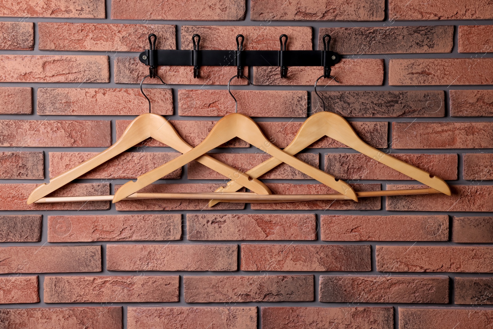 Photo of Hook rack with wooden clothes hangers on red brick wall