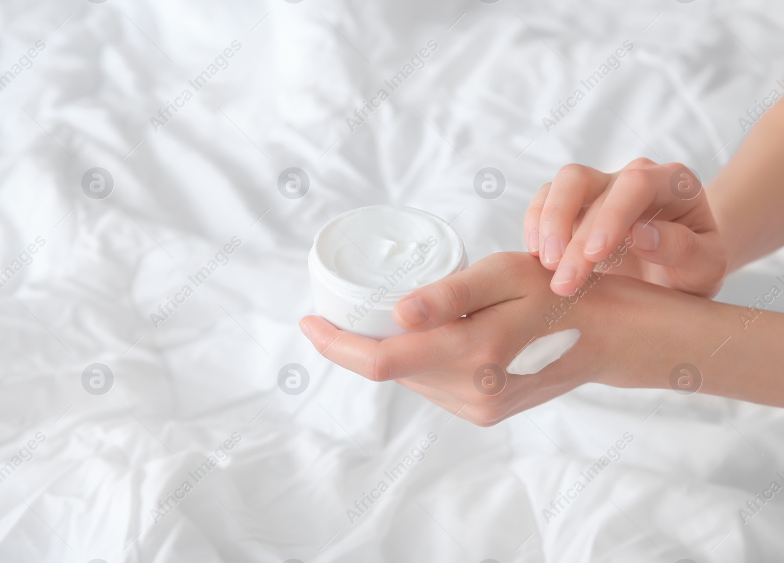 Photo of Young woman applying cream onto hands, indoors