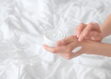 Young woman applying cream onto hands, indoors