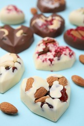 Tasty chocolate heart shaped candies with nuts on light blue background, closeup