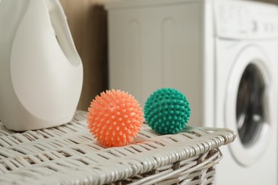 Photo of Dryer balls and laundry detergent on wicker basket near washing machine, closeup