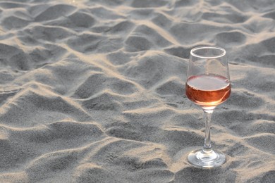 Photo of Glass of tasty rose wine on sand, space for text