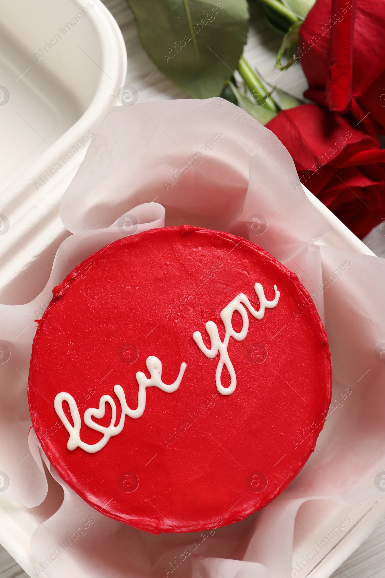 Photo of Bento cake with Love You text in takeaway box and roses on white wooden table, top view. St. Valentine's day surprise