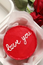 Bento cake with Love You text in takeaway box and roses on white wooden table, top view. St. Valentine's day surprise