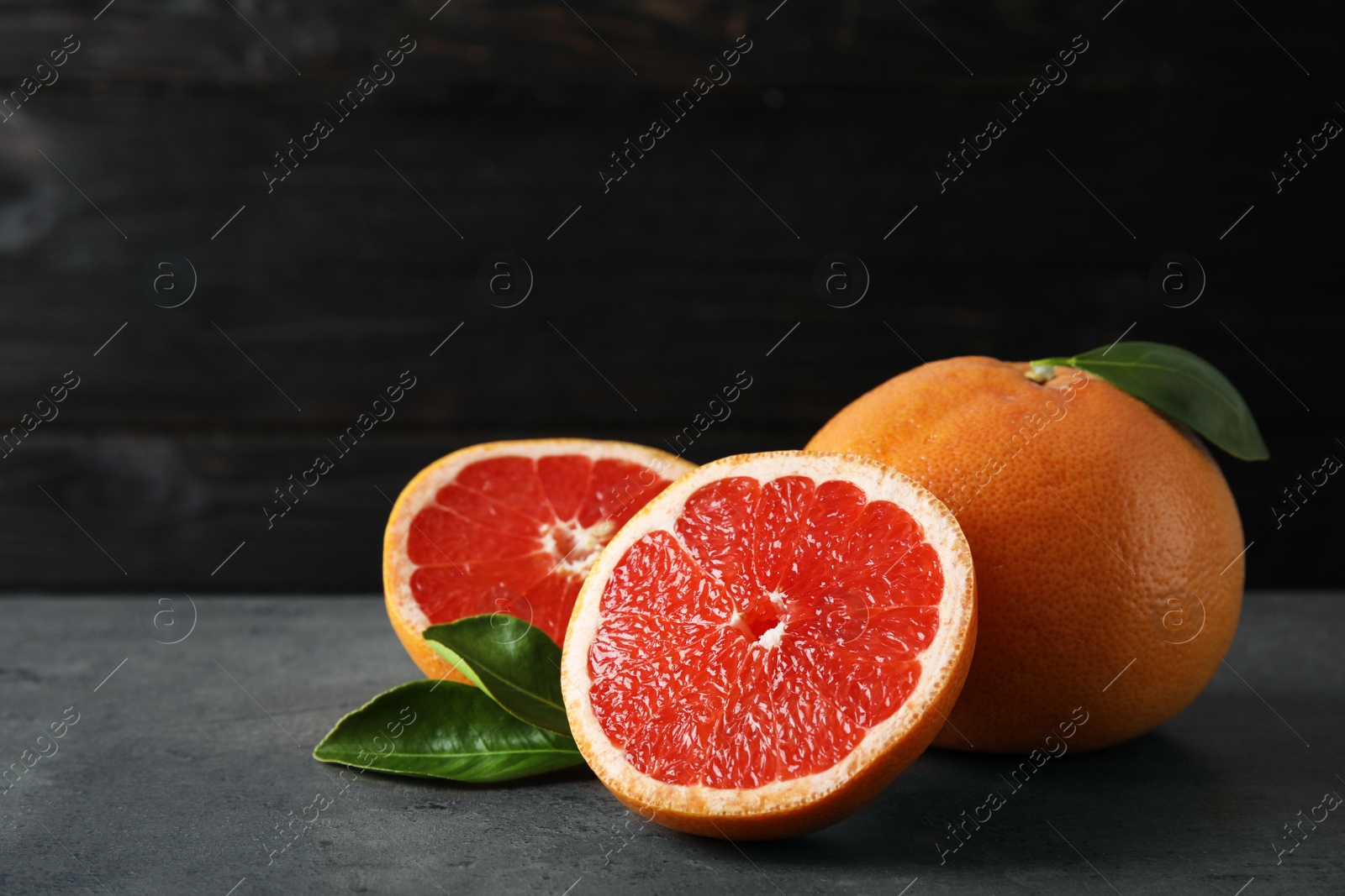 Photo of Fresh tasty grapefruits on table against black background. Space for text