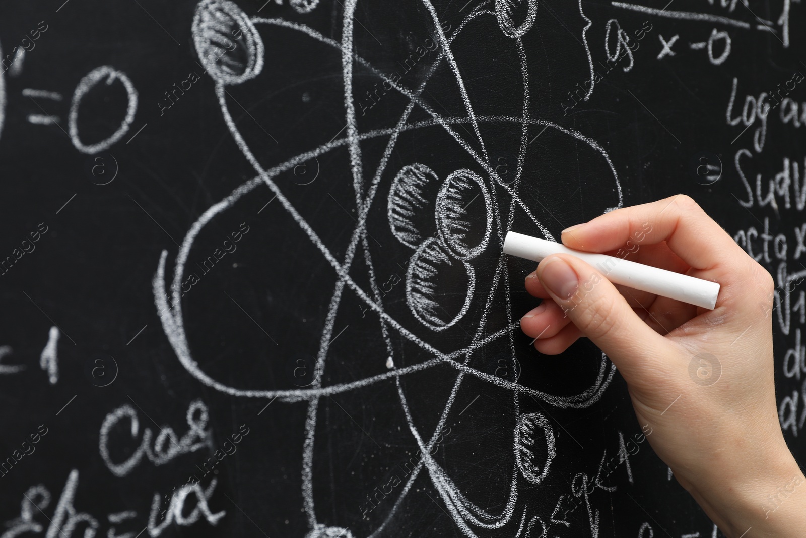 Photo of Teacher writing physical formulas with chalk on black chalkboard, closeup