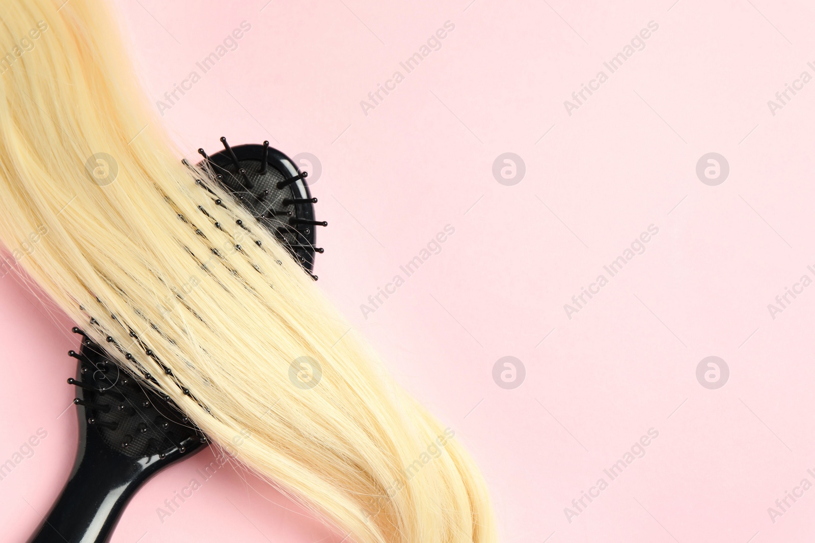 Photo of Stylish brush with blonde hair strand on pink background, top view. Space for text