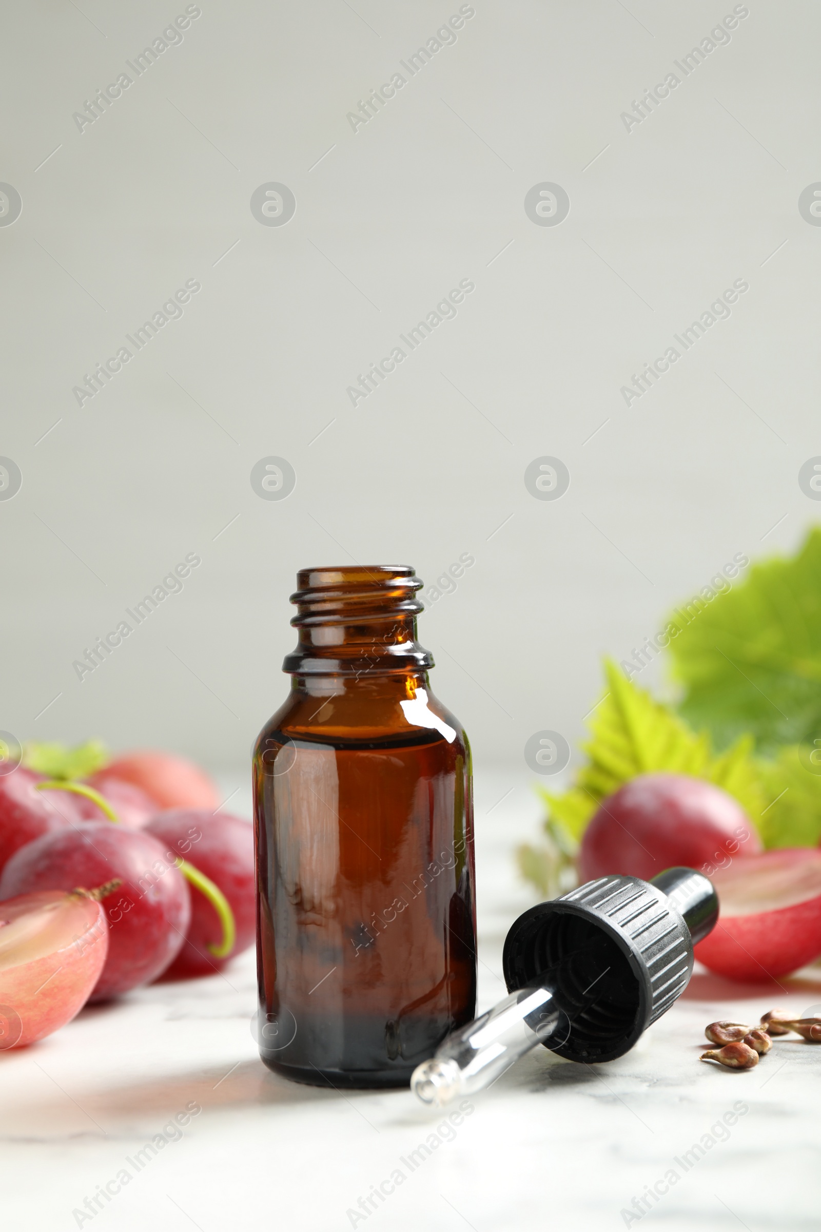 Photo of Bottle of natural grape seed oil on white marble table. Organic cosmetic