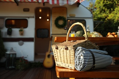 Photo of Wicker basket with picnic blanket on wooden bench near motorhome. Camping season