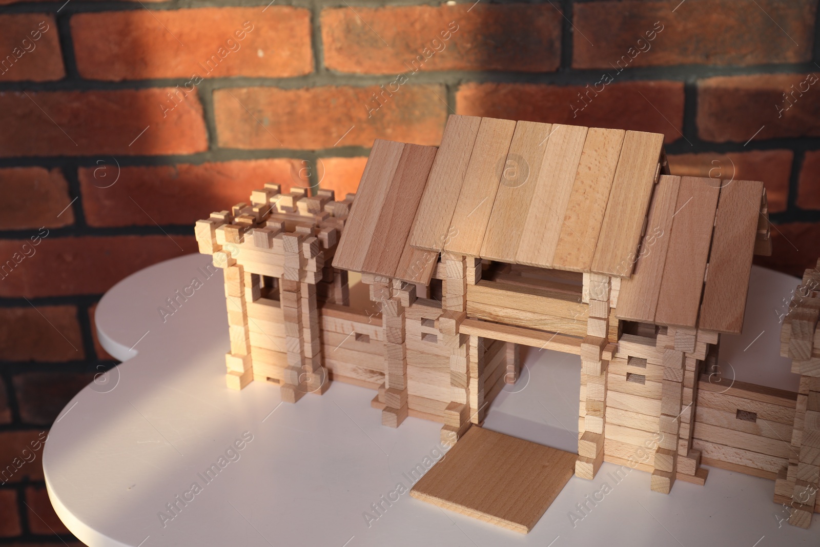 Photo of Wooden castle on white table near brick wall. Children's toy