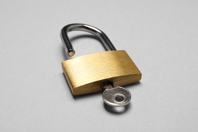 Steel padlock with key on grey background, closeup