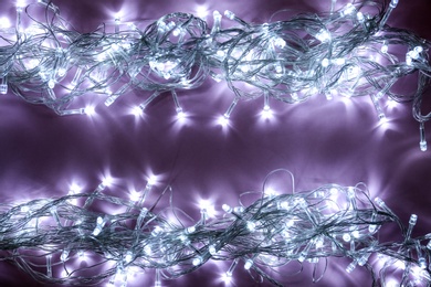 Photo of Glowing Christmas lights on violet background, top view