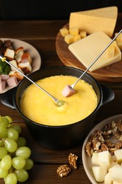 Photo of Fondue pot with melted cheese, forks and different products on wooden table