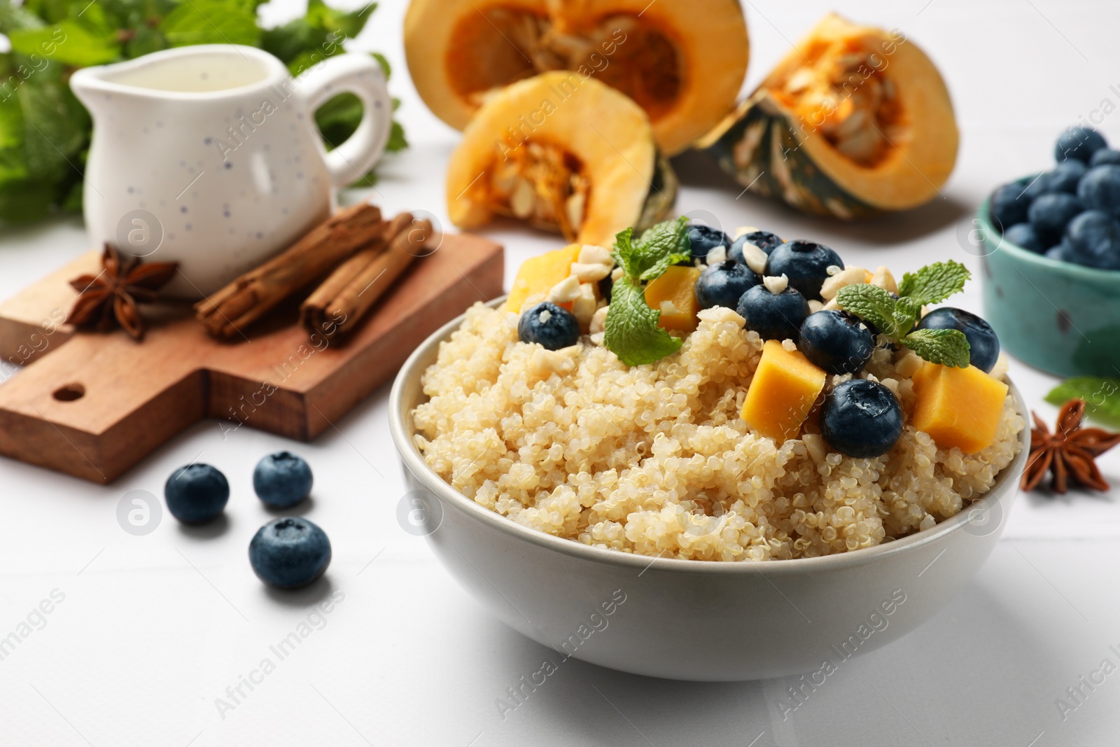 Photo of Tasty quinoa porridge with blueberries, pumpkin and mint in bowl on white table