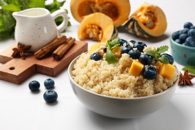 Photo of Tasty quinoa porridge with blueberries, pumpkin and mint in bowl on white table