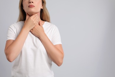 Photo of Young woman doing thyroid self examination on light grey background, closeup. Space for text