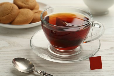 Photo of Tea bag in glass cup of hot water on white wooden table, closeup