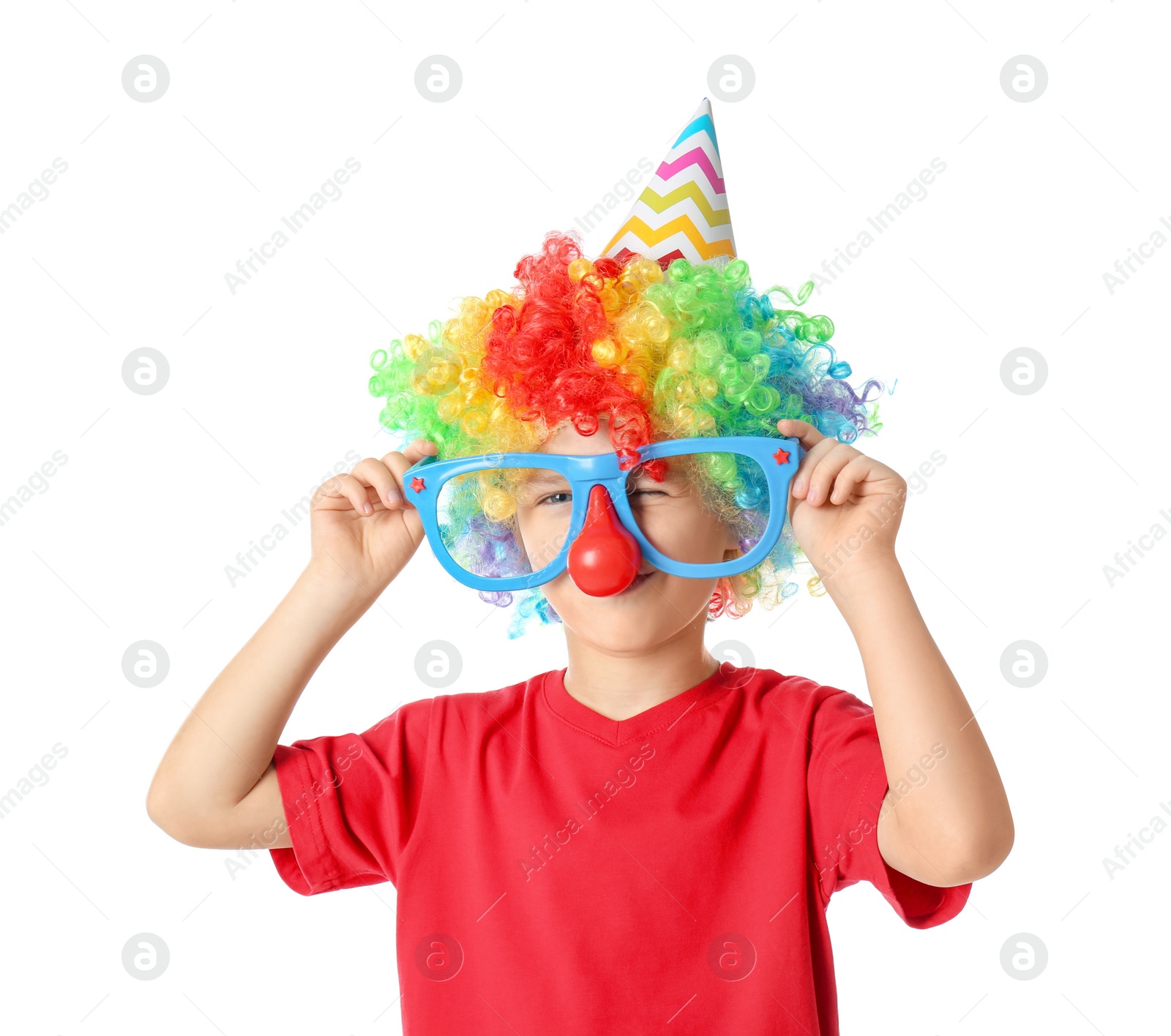 Photo of Little boy in clown wig, party hat and funny glasses on white background. April fool's day