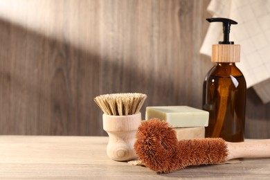 Photo of Cleaning brushes, dispenser and soap bars on wooden table, space for text