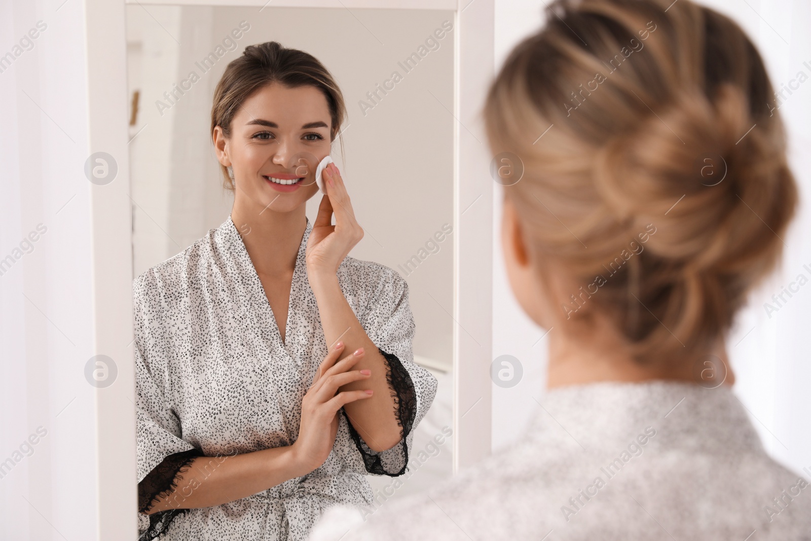 Photo of Beautiful young woman cleaning her face near mirror in room