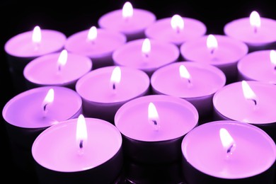 Beautiful burning violet candles on black background, closeup. Funeral attributes