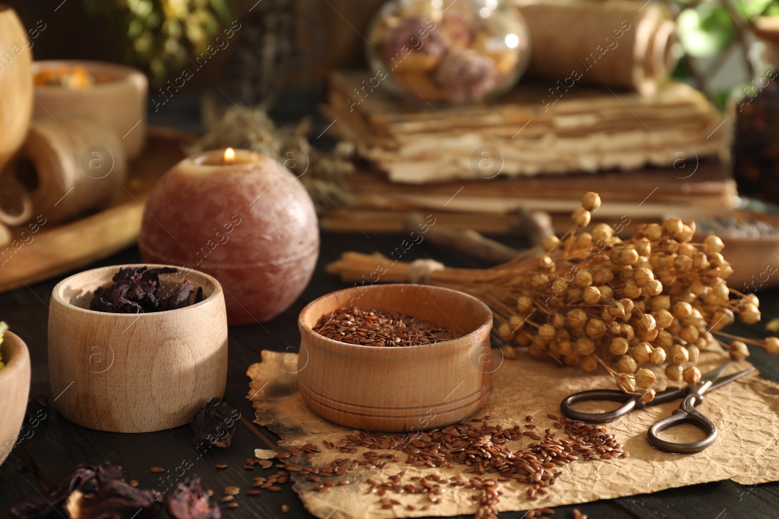 Photo of Different dry herbs, flowers, burning candle and scissors on black wooden table indoors