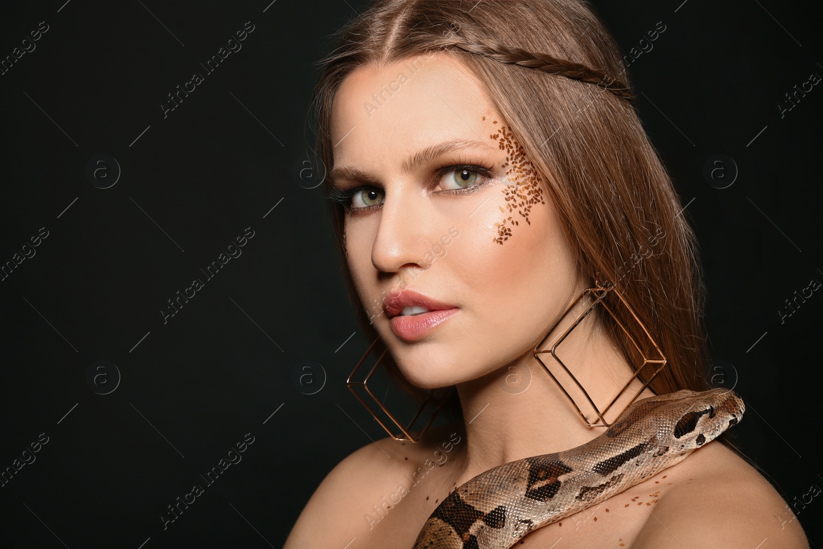 Photo of Beautiful woman with boa constrictor on black background, closeup